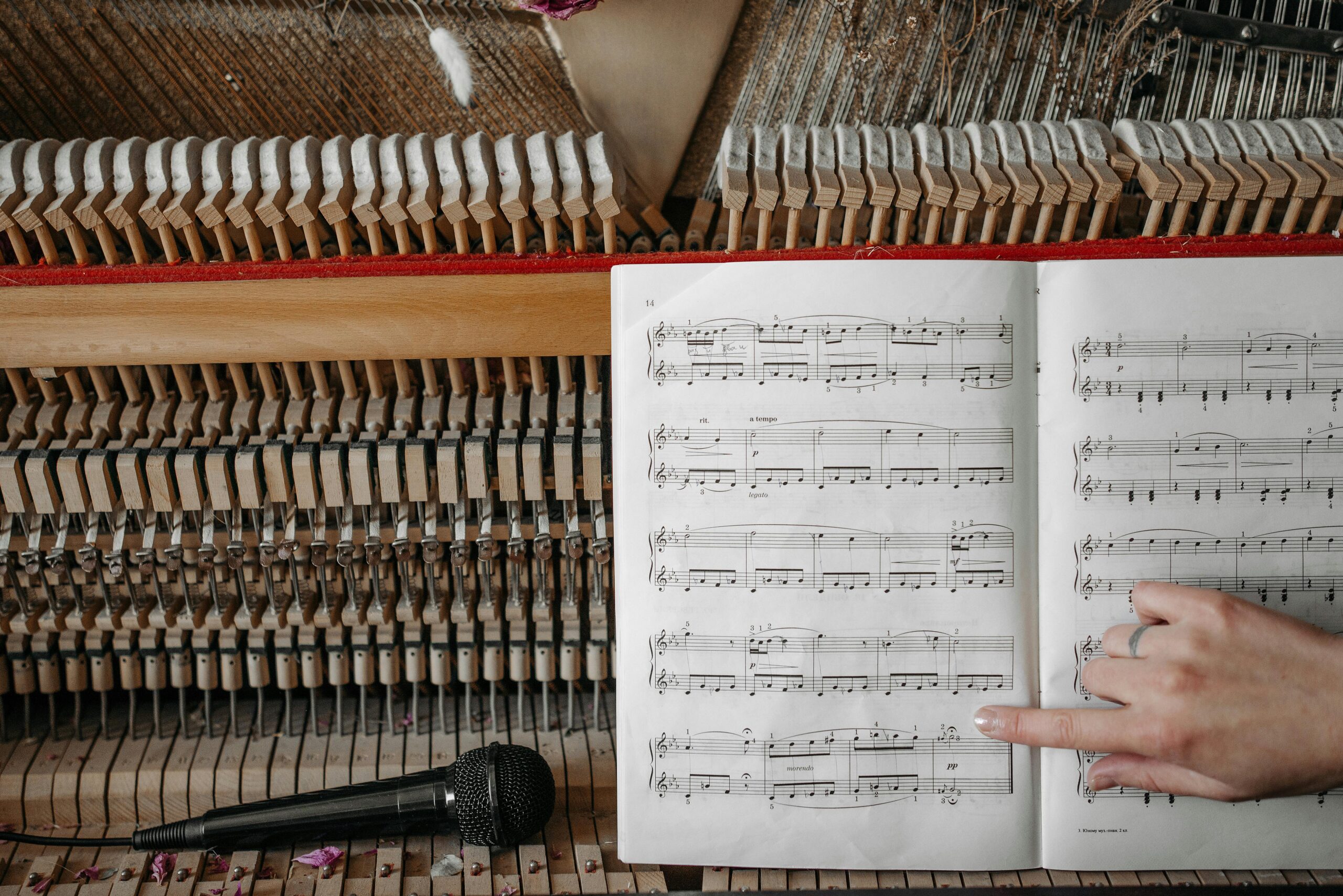 Closeup of piano interior and sheet music with hand pointing, microphone nearby.