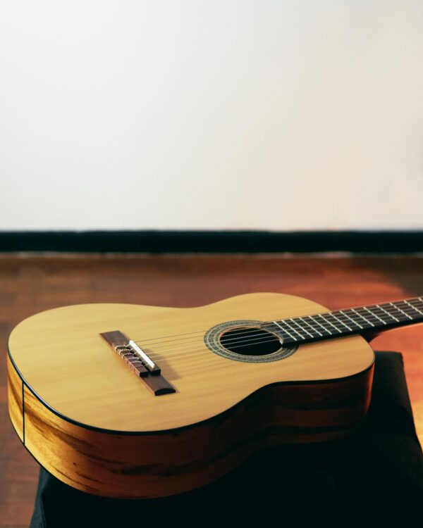 Warm-toned acoustic guitar resting on a wooden floor with dramatic lighting.
