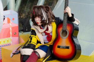 Anime cosplayer with guitar in colorful costume outdoors, blending music and Japanese pop culture.