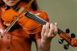 Close-up image of a child playing the violin indoors, focusing on the strings and hand.